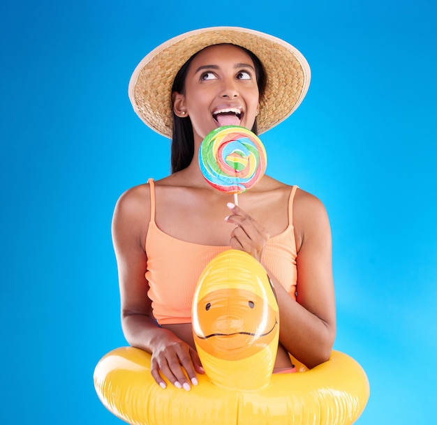 Piscina flutuante mulher feliz e pirulito lambendo em um estúdio com doce maiô e doces Fundo azul isolado e feriado de uma jovem fêmea com felicidade lambendo doces e sentindo-se engraçado ou bobo