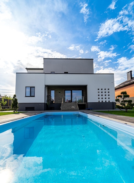 Piscina frente a casa rica. Agua limpia. Vista frontal del edificio. Vivienda actualizada con porche abierto y garaje. Arquitectura moderna.