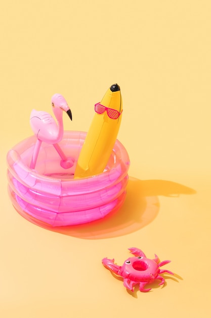 Piscina infantil com um inflável em forma de banana com óculos de sol e um flamingo inflável dentro e um caranguejo inflável