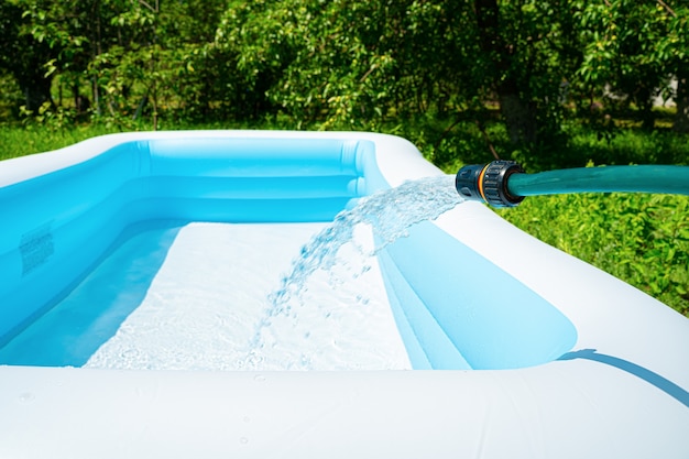 La piscina de jardín inflable se llena con agua de una manguera. Enfoque selectivo. Vista lateral, espacio para copiar.