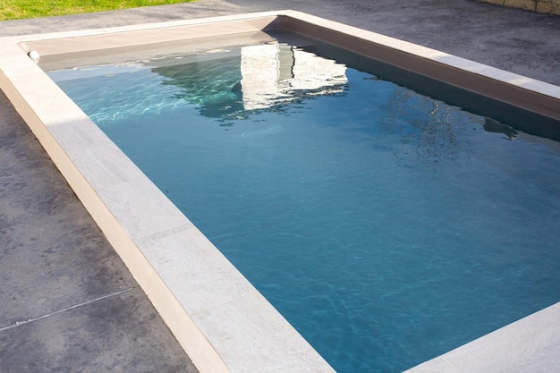 Piscina privada en casa familiar con revestimiento de piedra con terraza de hormigón encerado gris agua azul transparente