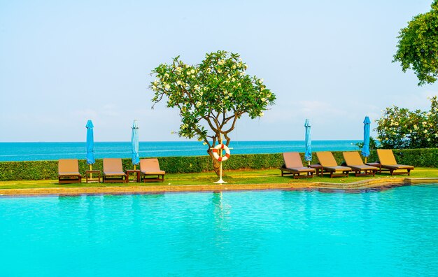 Piscina de sillas o piscina de cama y sombrilla alrededor de la piscina con fondo de mar - Vacaciones y concepto de vacaciones