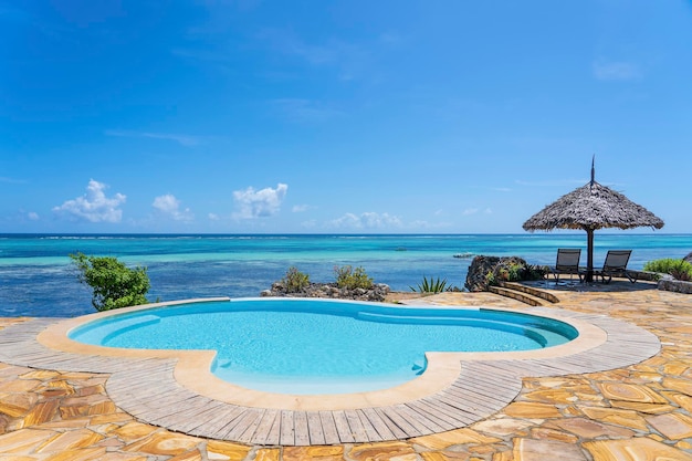 Piscina y sombrilla de paja en una playa tropical cerca del mar en un día soleado en la isla de Zanzíbar, Tanzania, África