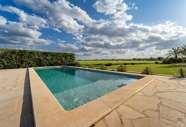 Piscina con vistas al jardín verde con cielo azul nublado