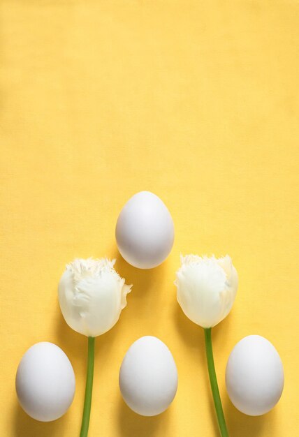 Piso minimalista de Pascua con huevos de Pascua y tulipanes blancos sobre un fondo amarillo