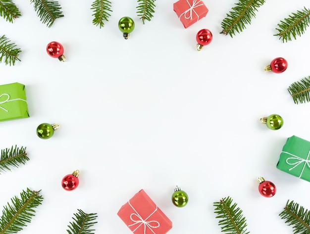 Piso de navidad con espacio de copia en el medio. ramas de árboles, adornos verdes y rojos, cajas de regalo sobre un fondo blanco.