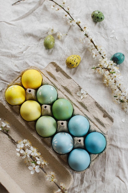 Piso rústico de pascua Huevos de pascua con estilo y rama de cerezo floreciente en mesa rústica Felices Pascuas Huevos pintados naturales en bandeja de papel y flor de primavera en tela de lino