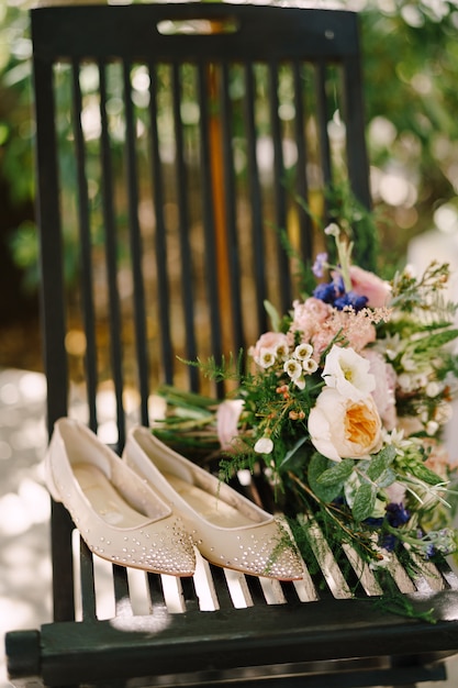 Pisos de novia cubiertos de pedrería en una silla junto a un ramo de flores