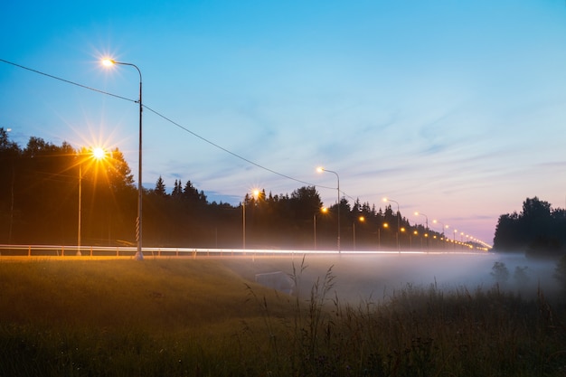 Pista de campo de noche con linternas y niebla.