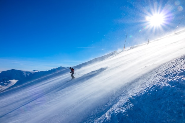 Pista de esquí empinada y sol brillante. Tormenta de nieve en la superficie. Esquiador baja