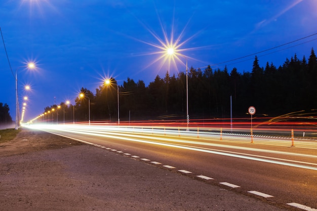 Pista noturna com lanternas e luzes desfocadas de carros em movimento.