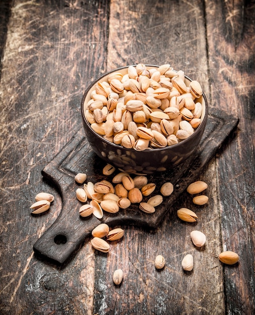 Pistachos en un cuenco sobre el tablero. Sobre fondo de madera.