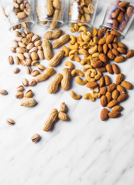 Foto pistachos derramados; maní anacardos y almendras de tarro sobre fondo de mármol