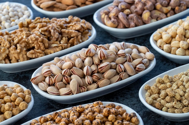 Pistachos en enfoque selectivo Nueces en un plato sobre un fondo oscuro Nuez Garbanzos Garbanzos blancos Pistacho seco de morera almendra anacardo Tipos de nueces en el plato