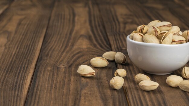 Pistachos fritos en una taza blanca sobre una mesa de madera. Fuente natural de proteínas y carbohidratos.