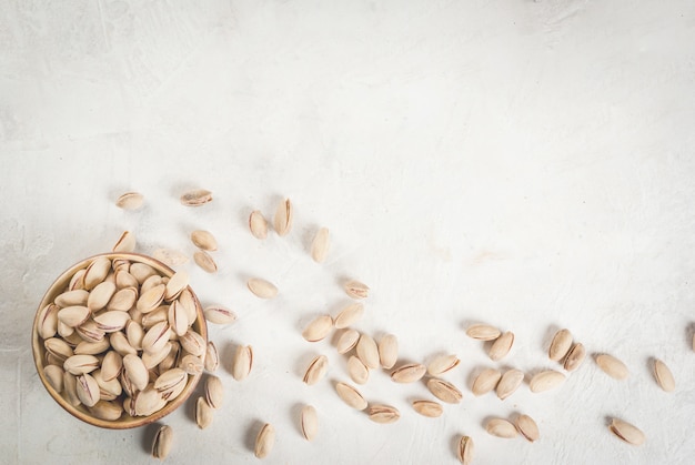 Pistachos en una mesa de piedra blanca, en un recipiente y dispersos. Copia espacio vista superior