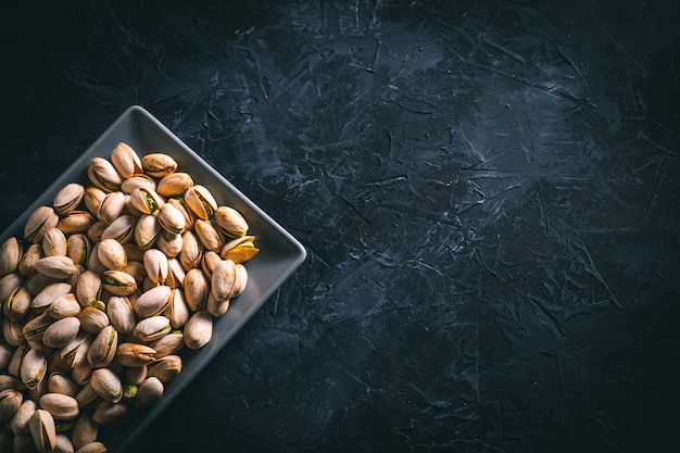 Foto pistachos en una placa rectangular gris sobre una mesa oscura