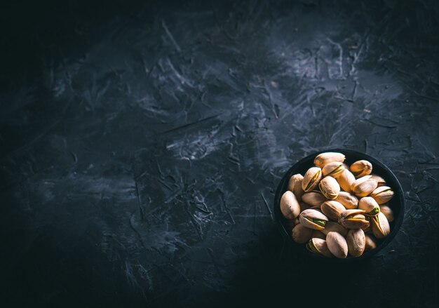 Foto pistachos en un recipiente oscuro sobre una mesa oscura