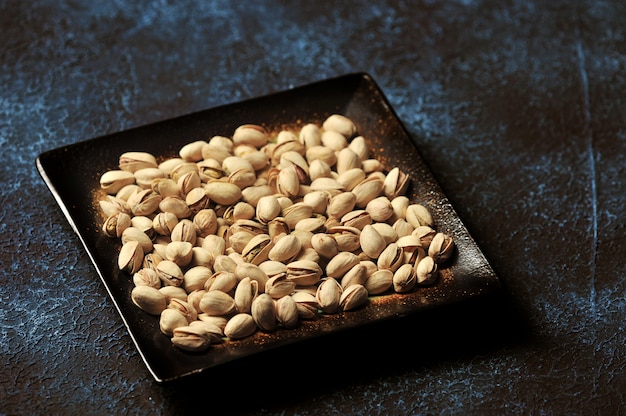 Pistachos en un recipiente sobre un fondo azul oscuro