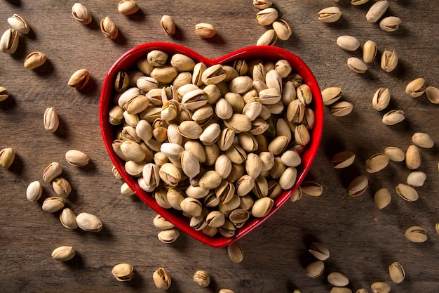 pistachos en un tazón de corazón con fondo de madera.