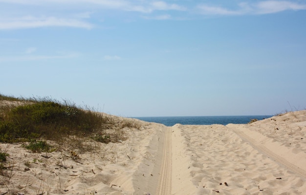Pistas de pneus na praia de areia contra o céu.