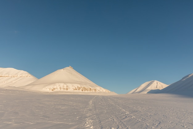 Pistas de motos de nieve en el paisaje del invierno ártico con montañas cubiertas de nieve en Svalbard, Noruega