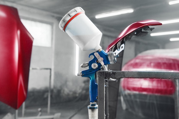 Pistola de aerógrafo en la cámara de pintura en el fondo de la parte pintada del coche Pintura de la parte de la carrocería del coche en la cámara