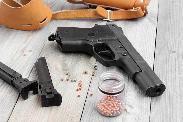 Pistola de aire, dos clips, pistolera y bolas para disparar a una mesa de madera.