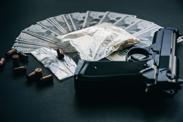Pistola con balas sobre la mesa. Problemas criminales. Drogas y dinero sobre fondo negro. Venta ilegal.