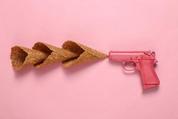 Pistola con conos de gofres de helado sobre fondo rosa Concepto de fiesta mínimo Diseño creativo