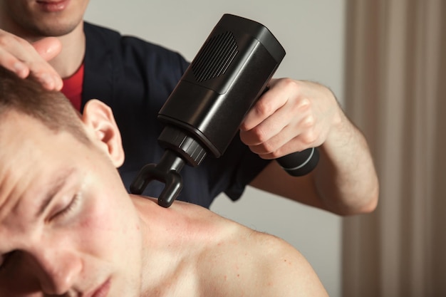 Pistola de cuello masaje de percusión muscular hombre atlético en sala médica