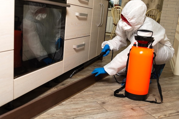 Pistola de pulverização com pesticidas closeup Um exterminador em roupas de trabalho pulveriza pesticidas de um frasco de spray Luta contra insetos em apartamentos e casas Desinsetização de instalações