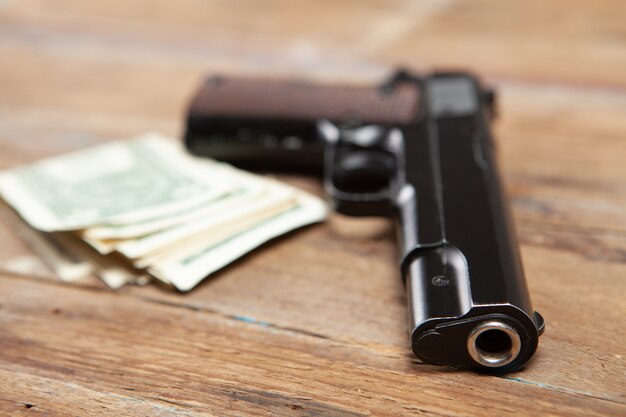 Pistola negra y dinero en una mesa de madera