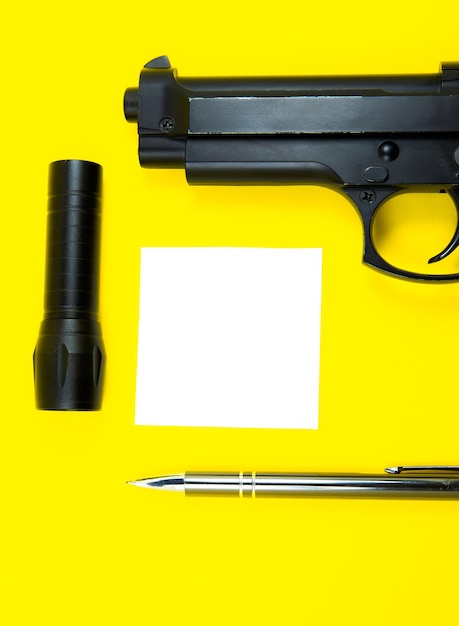 La pistola negra, el papel de nota recordatorio, el bolígrafo y la linterna se encuentran sobre un fondo amarillo. Los detectives privados trabajan. Concepto de búsqueda de información.