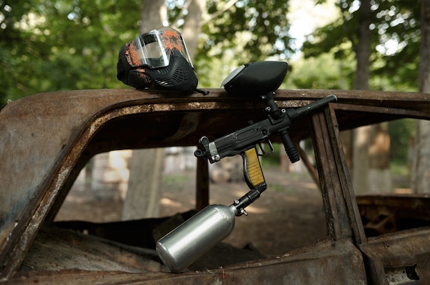 Pistola de paintball y primer plano de la máscara de protección, nadie, parque infantil en el bosque en el fondo. Deporte extremo al aire libre, armas neumáticas y balas de pintura, concepto de juego de equipo militar