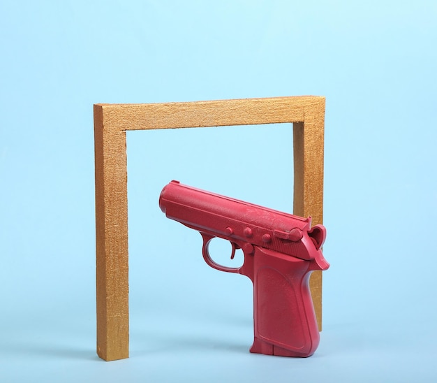 Foto pistola rosa con arco de marco dorado sobre fondo azul minimalismo naturaleza muerta arte conceptual