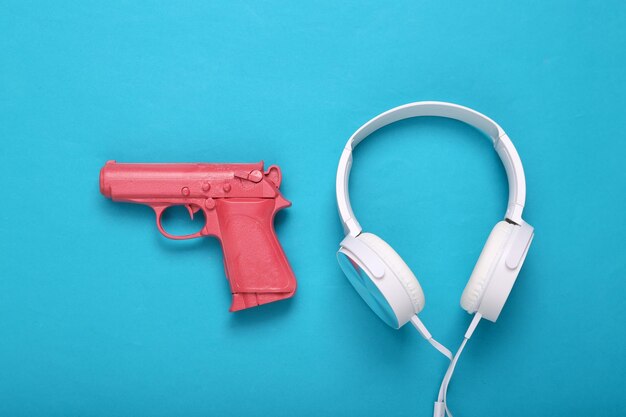 Pistola rosa con auriculares sobre fondo azul Concepto creativo Minimalismo Plano Lay Diseño mínimo Vista superior