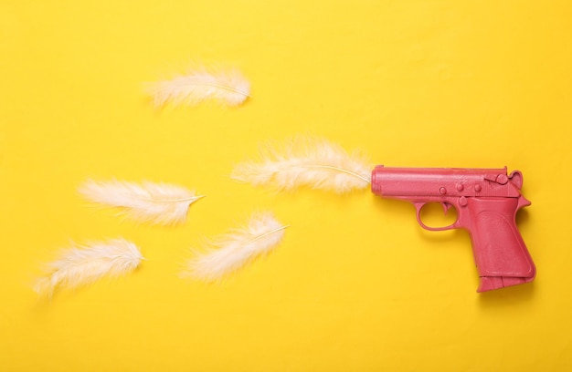 Pistola rosa con plumas sobre fondo amarillo Concepto creativo Minimalismo Plano Diseño mínimo Vista superior