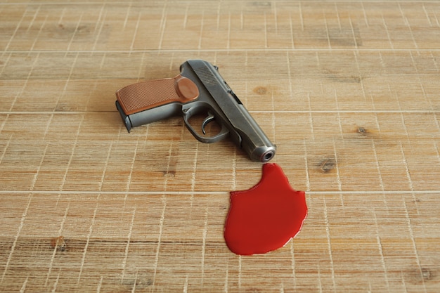 Pistola y sangre escarlata sobre tabla de madera.