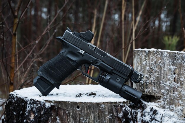 Pistola táctica de 9 mm con mira de punto rojo, linterna de freno en el bosque de invierno