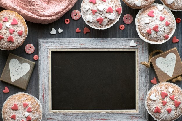 Foto pizarra enmarcada con magdalenas cubiertas de azúcar con corazones de glaseado de fondant rosa y blanco