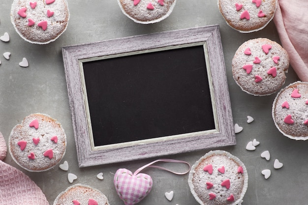 Pizarra enmarcada con magdalenas salpicadas de azúcar con corazones de glaseado de fondant rosa y blanco