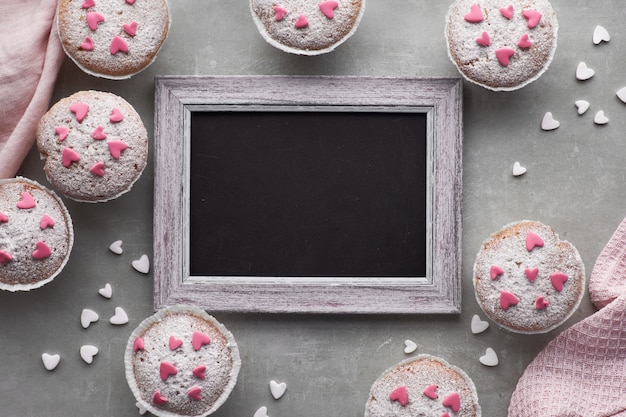 Pizarra enmarcada con magdalenas salpicadas de azúcar con corazones de glaseado de fondant rosa y blanco