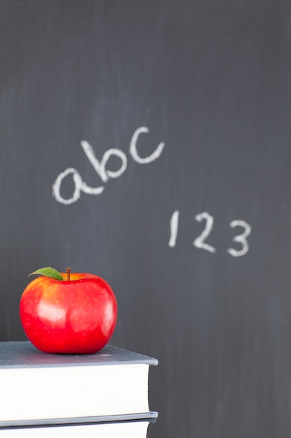 Pizarra con figuras y letras y una manzana y libros.