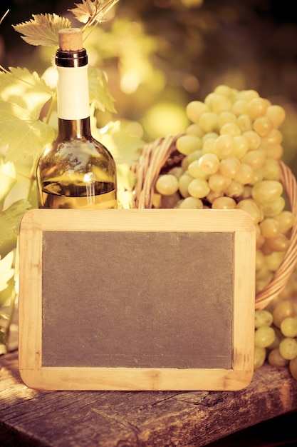 Pizarra de madera en blanco, botella de vino y uvas de vid en otoño
