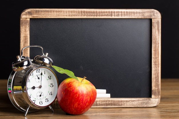 Pizarra y manzana roja cerca de un reloj