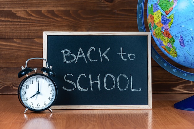 Una pizarra con el texto Regreso a la escuela, un reloj despertador y un globo terráqueo sobre un fondo de madera