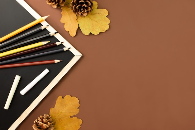 Pizarra, tiza, lápices de colores, conos, hojas en marrón
