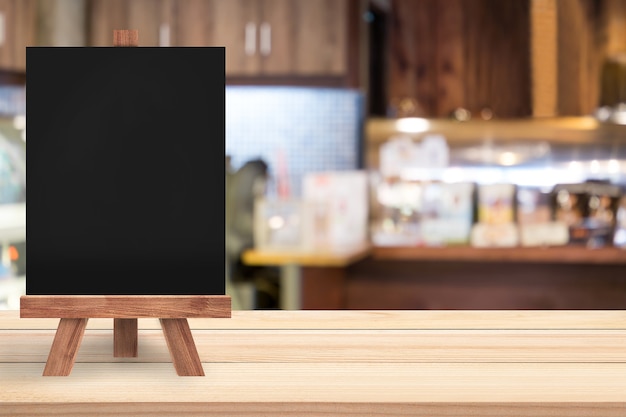 Una pizarra vacía con caballete está en una mesa de madera en un restaurante / cafetería