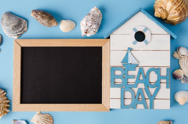 Pizarra vacía con conchas y día de playa de inscripción en azul.